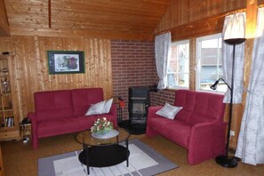 Ein Holzinnenraum mit zwei roten Sofas, einem Kamin und einem Fenster mit Vorhängen.