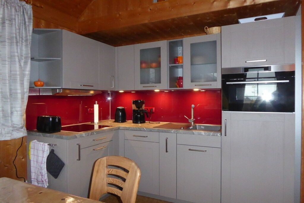 A compact kitchen with a red backsplash, a coffee maker, and a microwave.