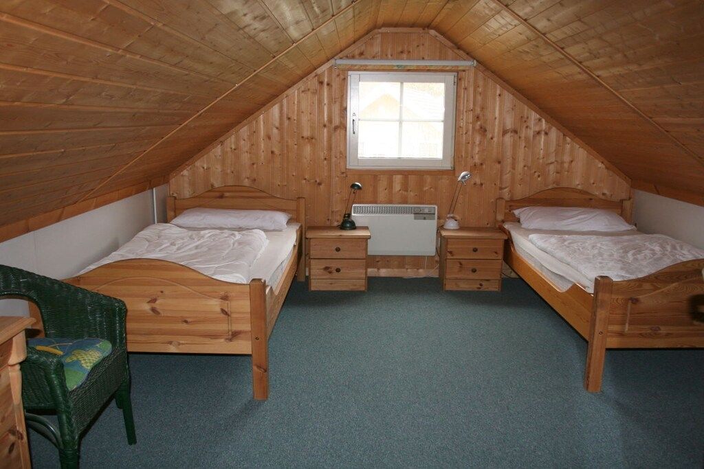 A small, attic-style bedroom with two wooden beds, a desk, and a window.