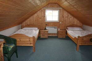 Ein kleines Schlafzimmer im Dachgeschoss mit zwei hölzernen Betten, einem Schreibtisch und einem Fenster.