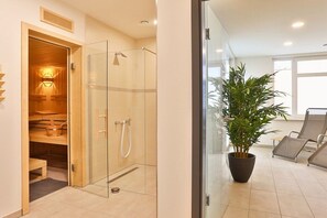 A modern bathroom with a glass shower enclosure, a wooden sauna room, and a potted plant. - ||---------------------------"Smells like the sea"----------------------|| (Glowe)