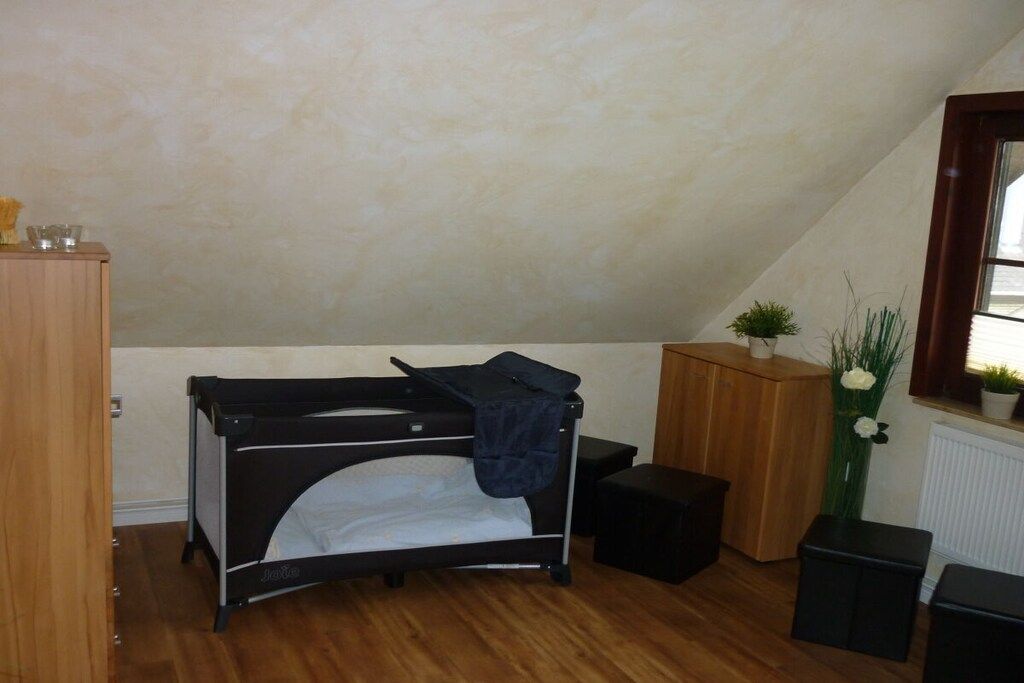 Quarto pequeno com beliche, um armário de madeira, uma planta em vaso e radiador.