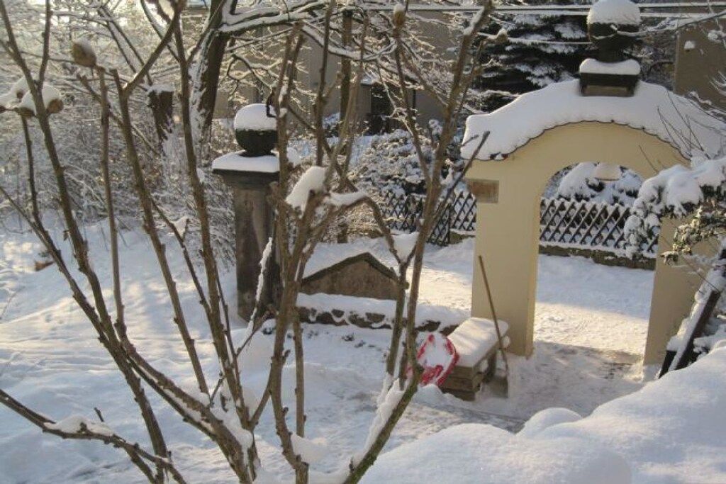 A snow-covered gate with a fence, a small shed, and bare trees.