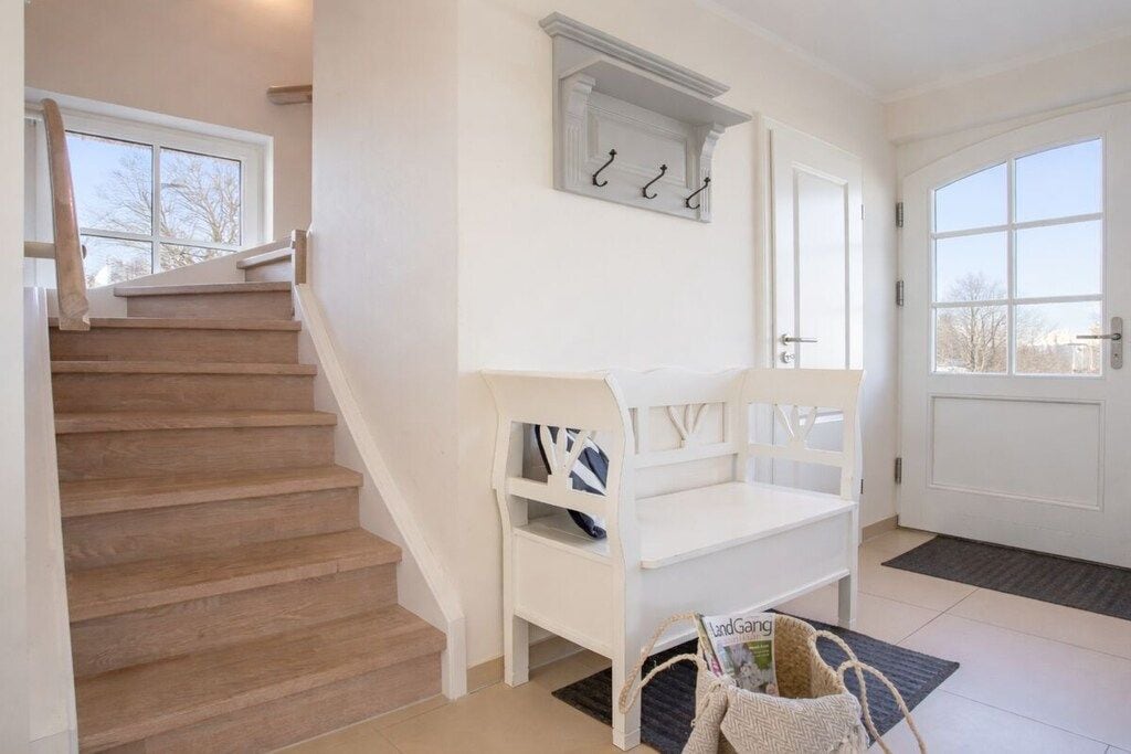 Un escalier menant à un palier où se trouvent un banc blanc et un porte-manteau.