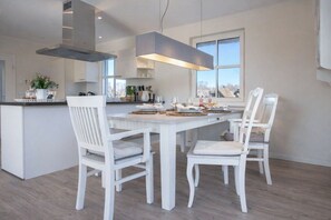 A modern kitchen with white cabinetry, a central island, and a dining area with white chairs. - Holiday home with 3 bedrooms (Fuhlendorf)