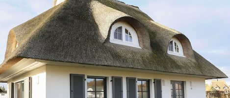 A house with a thatched roof, white walls, and multiple windows with shutters.