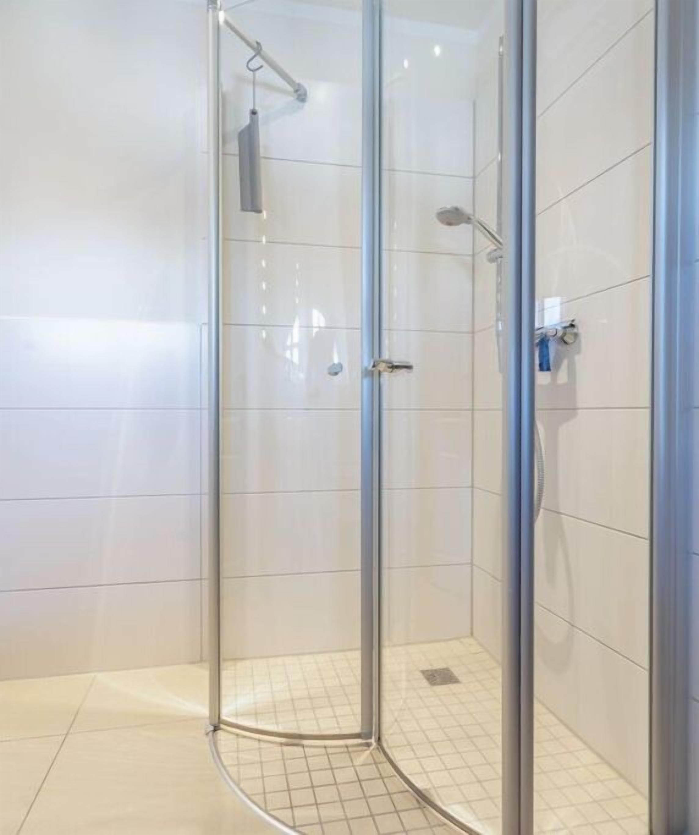 Eine gläserne Duschkabine mit Handbrause und am Wand montiertem Wasserhahn.