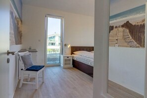 A bedroom with a bed, a chair, a nightstand, a door leading to a balcony, and a painting on the wall. - Holiday apartment in Glowe with swimming pool (Glowe)