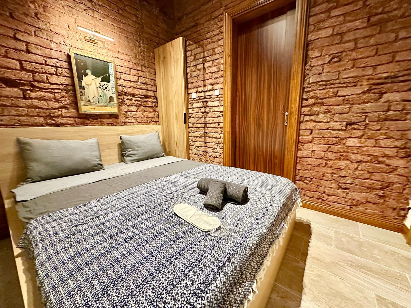 Ein Schlafzimmer mit Backsteinwand, Holztür, einem Bett mit gemustertem Überwurf und einem gerahmten Bild an der Wand.