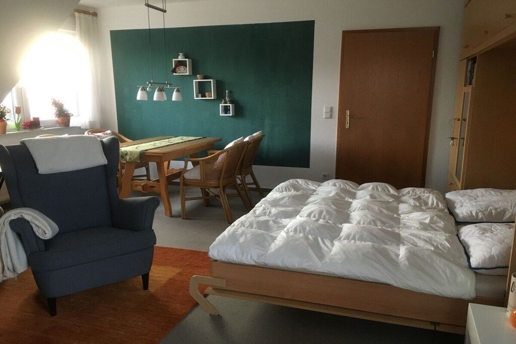A room with a bed, a chair, a table, and a door.