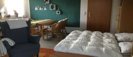 A room with a bed, a chair, a table, and a door.