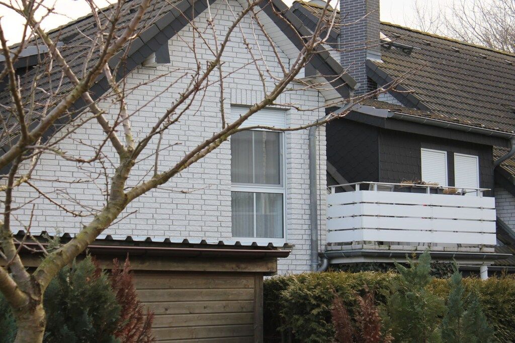 Een woongebouw met een witte bakstenen gevel, een grijs dak en een houten omheining.