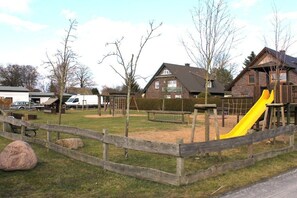 Ein Spielplatz mit einer gelben Rutsche, umgeben von einem Holzzaun, und Häusern im Hintergrund.