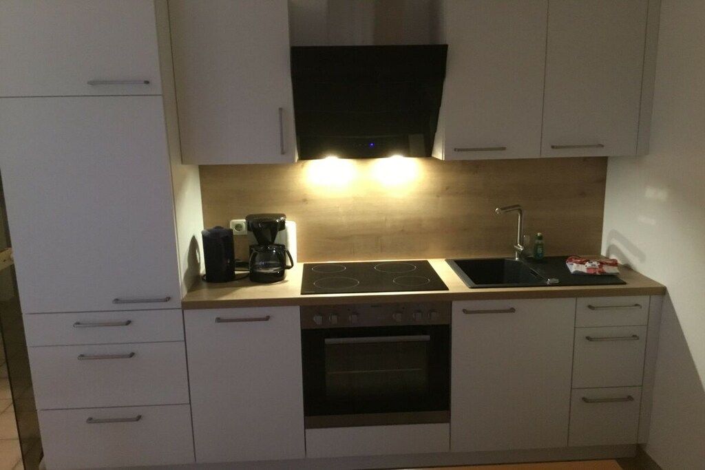 Eine Küche mit weißen Schränken, einem schwarzen Herd, einer Spüle und einer Kaffeemaschine.