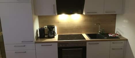 Cozinha com armários brancos, fogão preto, pia e cafeteira.