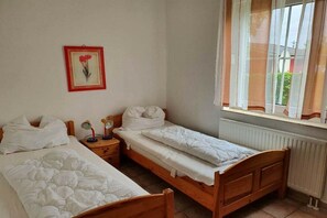 Ein Schlafzimmer mit zwei Einzelbetten, einem Nachttisch mit Lampe, einem gerahmten Bild an der Wand und einem Fenster mit Vorhängen.
