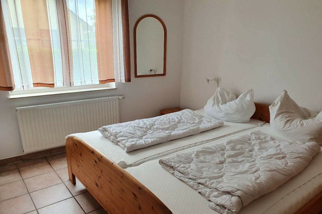 A bedroom with two beds, a radiator, a window with curtains, and a mirror on the wall.