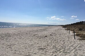 Ein sandiger Strand mit blauem Himmel und ruhigem Meer.