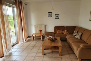 Ein Wohnzimmer mit einem braunen Sofa, einem Holztisch, einer Heizung und einem Fenster mit Vorhängen.