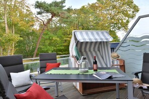 A deck with outdoor furniture, a table with a bottle and glasses, and a striped awning. - Holiday apartment with 2 bedrooms (Breege\/Juliusruh OT Juliusruh)
