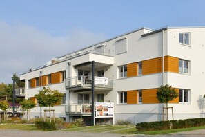 Moderni, useita kerroksia korkea asuinkerrostalo, jossa on parvekkeet, kyltti, joka osoittaa, että kyseessä on vuokra-asunto, sekä maisemoitu puutarha-alue.