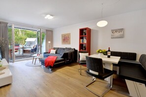 A modern living room with a sofa, a dining table, and a bookshelf. - Holiday apartment with 2 bedrooms (Breege\/Juliusruh OT Juliusruh)