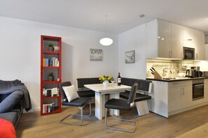 A modern living space with a dining area, kitchenette, and a bookshelf. - Holiday apartment with 2 bedrooms (Breege\/Juliusruh OT Juliusruh)