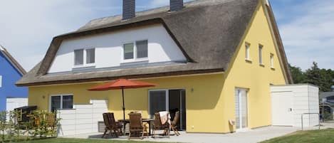Una casa con techo inclinado, un patio con mobiliario exterior y un área de juegos pequeña con una pelota y un carrito de juguete.