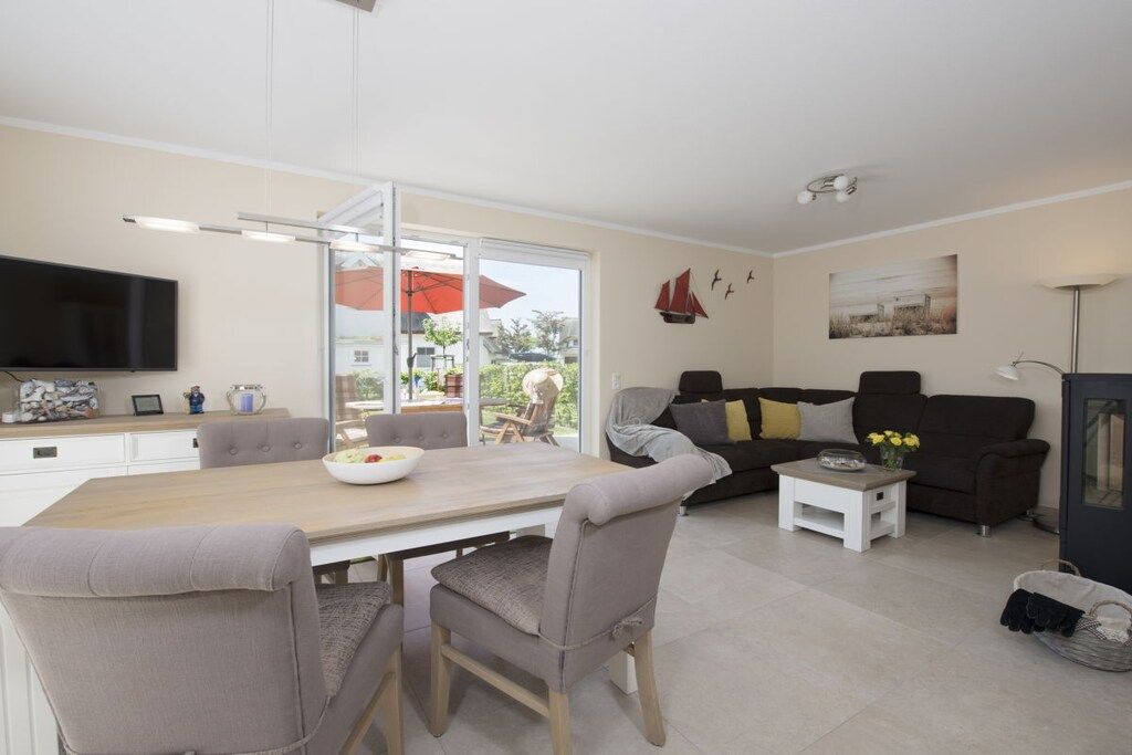 A modern living room with a dining area, a flat-screen TV, and a large window with a view of the outdoors.