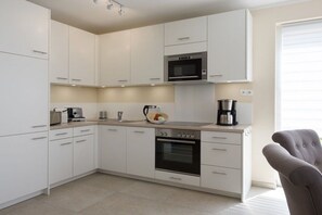 A modern kitchen with white cabinetry, a built-in microwave, a stove, and a coffee maker. - Holiday home in Breege with swimming pool (Breege)