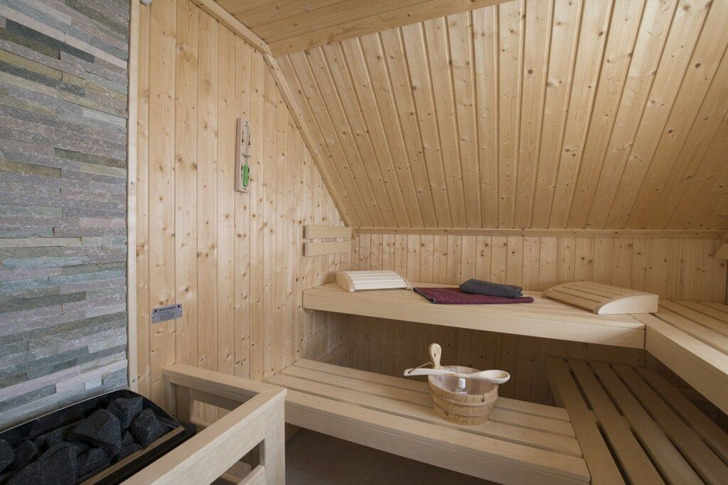 Eine Holzsauna mit Bänken und einer Steinwand.