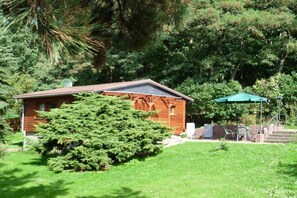 A cabin with a sloped roof, surrounded by dense greenery and a small patio area with outdoor furniture. - Holiday home with 1 bedroom (Diera-Zehren \/ OT Nieschütz)
