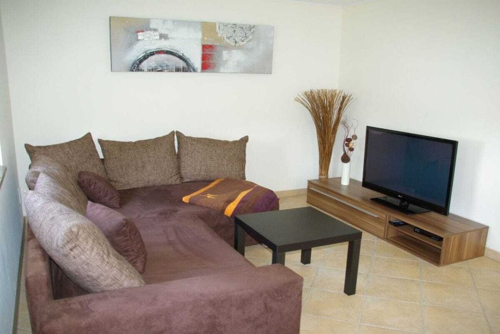 Een woonkamer met een bank, een salontafel, een televisie op een houten dressoir en een decoratieve vaas.
