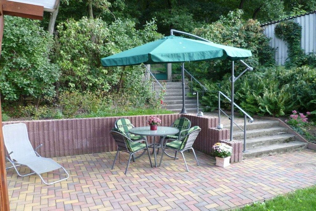 Une terrasse avec une table et des chaises, un parasol vert et un escalier menant à un niveau supérieur.