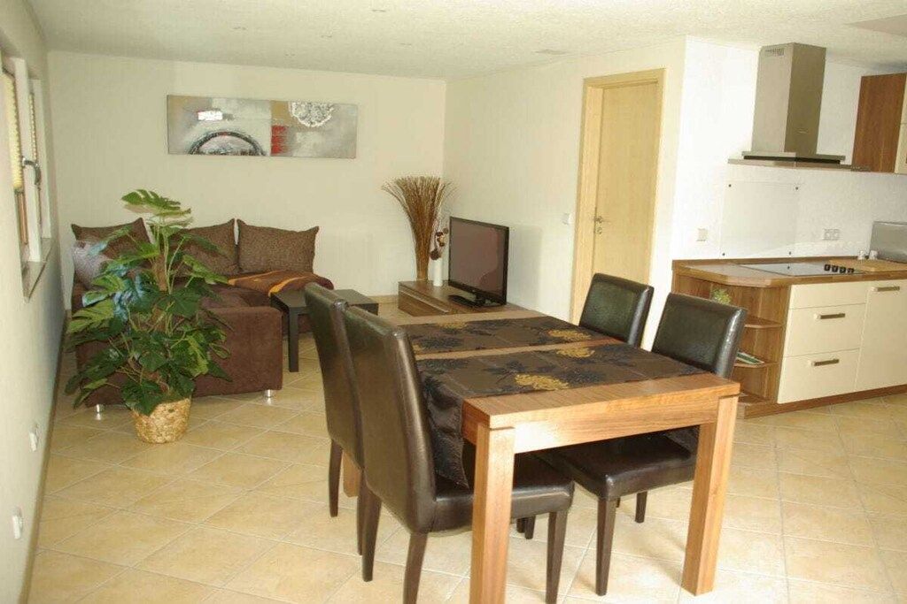 A dining area with a wooden table and chairs, a television, and a kitchen area with cabinets and a stove.