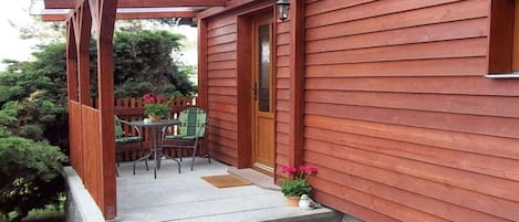 Eine Holzwand mit überdachter Veranda, einer Tür und einem kleinen Tisch mit Stühlen.