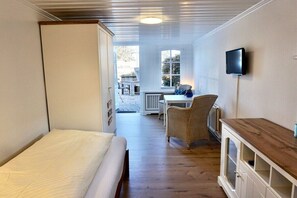 A room with a bed, a television, a wicker chair, and a small table. - Holiday apartment with 1 bedroom (Wenningstedt-Braderup)