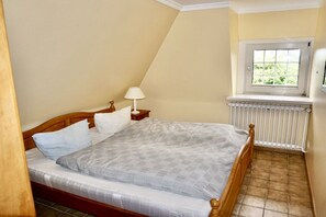 A bedroom with a single bed, a nightstand, a lamp, a window with a view, and a radiator. - Friesenhaus Carl Jensen Holiday Apartment 2 (Wenningstedt-Braderup)