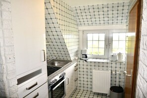 A compact kitchen with a stove, sink, and a window above the countertop. - Friesenhaus Carl Jensen Holiday Apartment 2 (Wenningstedt-Braderup)