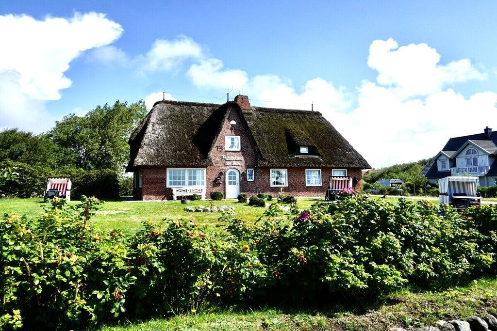A traditional brick house with a thatched roof, a small porch, and a well-maintained garden.