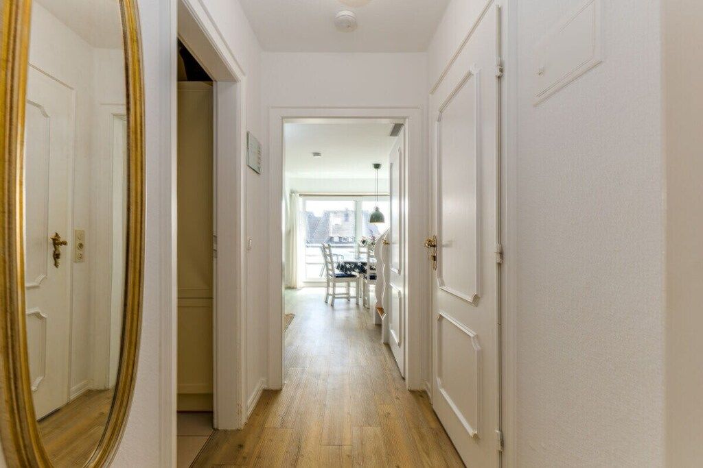 A hallway with a wooden floor, white doors, and a dining area in the distance.