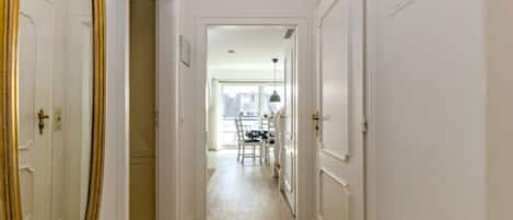 A hallway with a wooden floor, white doors, and a dining area in the distance.