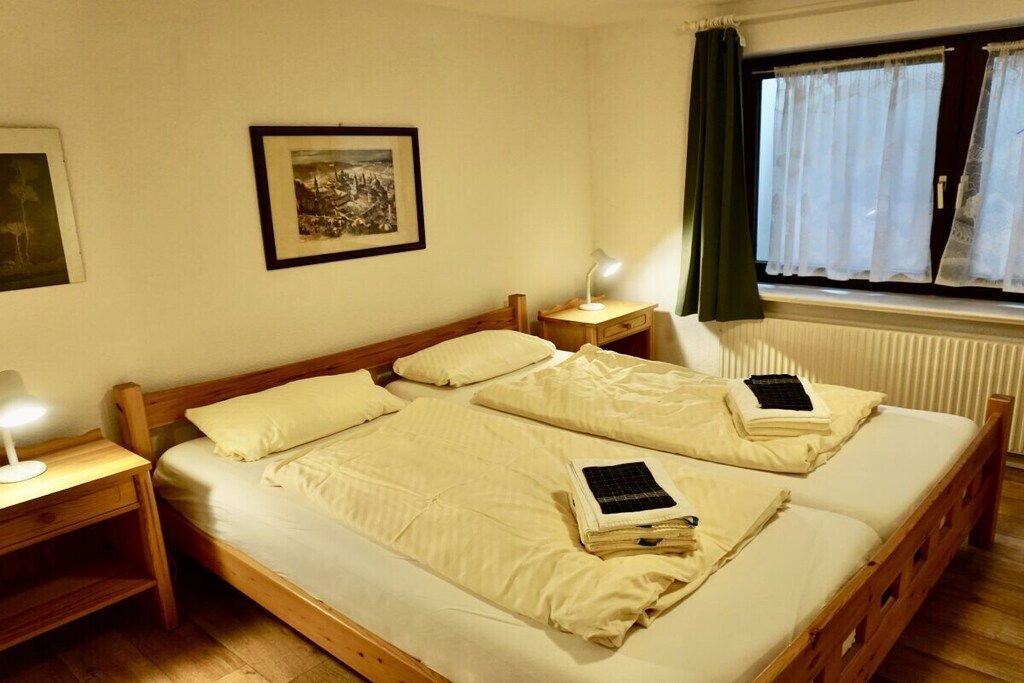A double bed with a wooden frame, two bedside tables with lamps, a framed picture on the wall, and a window with curtains.