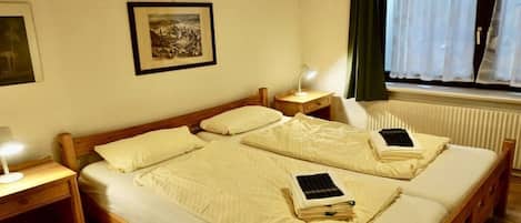 A double bed with a wooden frame, two bedside tables with lamps, a framed picture on the wall, and a window with curtains.