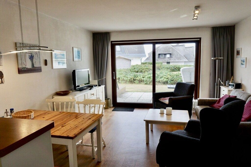 A living room with a wooden table, white chairs, a sofa, and a television.