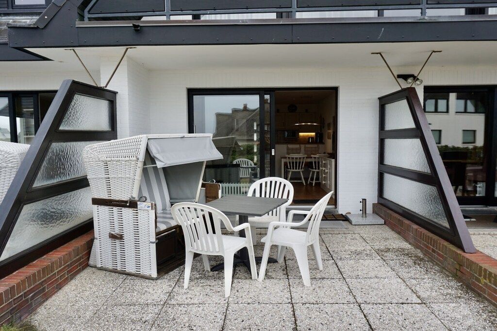 Eine Außenpatio mit Tisch, Stühlen und einem Korbsessel, sowie eine Glastür zu einem Innenraum.