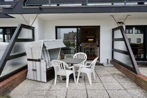 Eine Außenpatio mit Tisch, Stühlen und einem Korbsessel, sowie eine Glastür zu einem Innenraum.