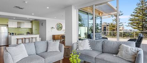 A modern living room with a grey sectional sofa, a coffee table with a vase, and a kitchen in the background.