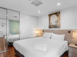 Une chambre d’hôtel avec un grand lit, une table de chevet, un miroir et une lampe fixée au mur.
