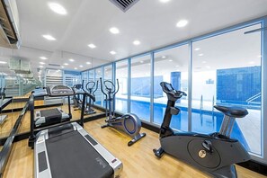 A gym with various exercise machines, large windows, and a view of a building outside. - Ocean Breeze - Stylish 2 Bedroom with terrace - 3-minute walk to beach (Glenelg)